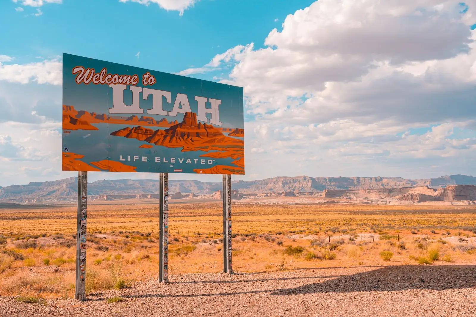 A "Welcome to Utah" sign in the desert under a cloudy sky.